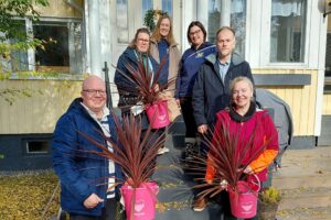 Asumiskokeilijat, Pomarkun kunnanjohtaja ja Palvelusihteeri-kirjastovirkailija, sekä hanketyöntekijät yhteiskuvassa Villa Rouheen ulkorappusilla. Käsissä asumiskokeilijoilla lahjaksi saadut pinkit ämpärit joissa pinkit kukat.