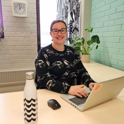 Etätyöntekijä Pomarkun uusissa etätyötiloissa tekemässä töitä kannettavalla tietokoneella. Sivuseinä on maalattu vaalean turkoosiksi kunnan brändivärien mukaan.