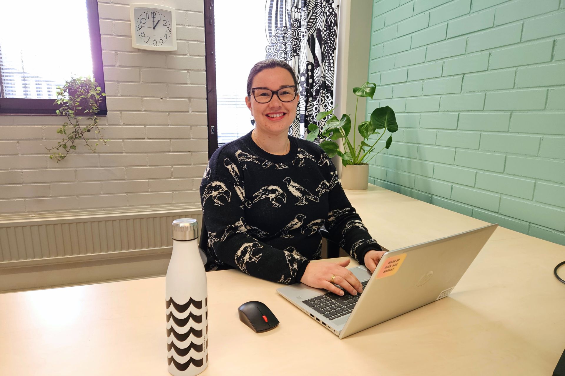 Etätyöntekijä Pomarkun uusissa etätyötiloissa tekemässä töitä kannettavalla tietokoneella. Sivuseinä on maalattu vaalean turkoosiksi kunnan brändivärien mukaan.